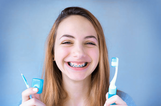 Girl with braces holding toothbrush and floss